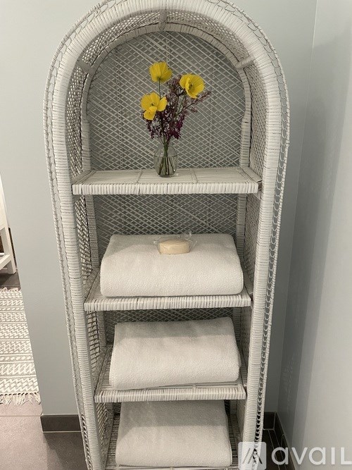 A white shelf with towels and a vase of flowers.