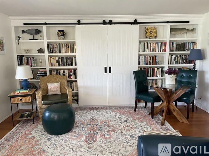 A living room with a rug, a chair, a table, and a bookshelf.