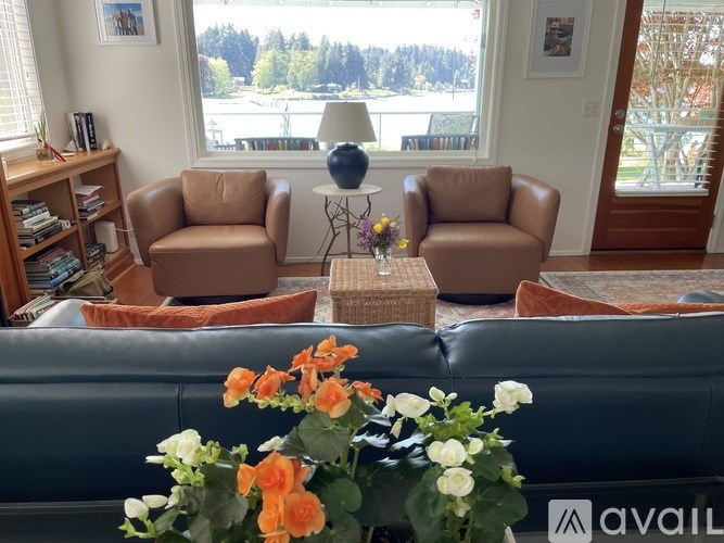 A living room with a couch, two chairs, a table with flowers, and a view of trees outside the window.