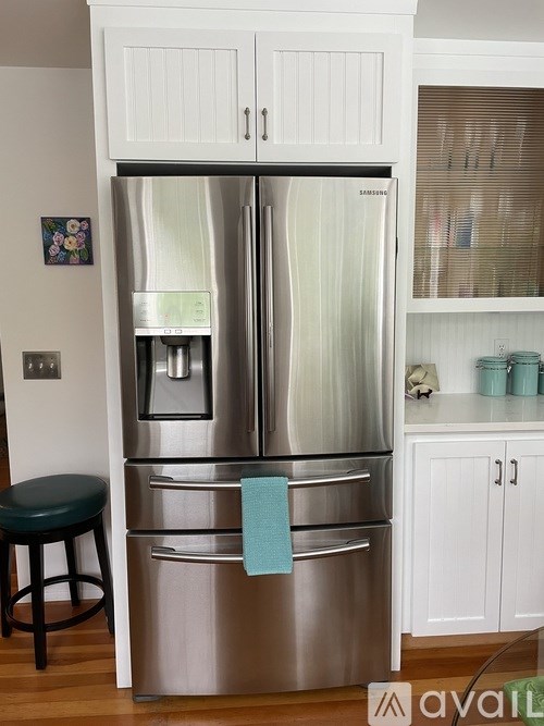 A stainless steel refrigerator with a black stool in front of it.