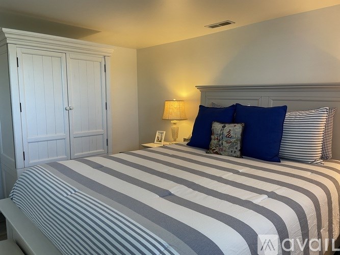 A bed with a striped comforter and blue pillows is in a room with white walls.