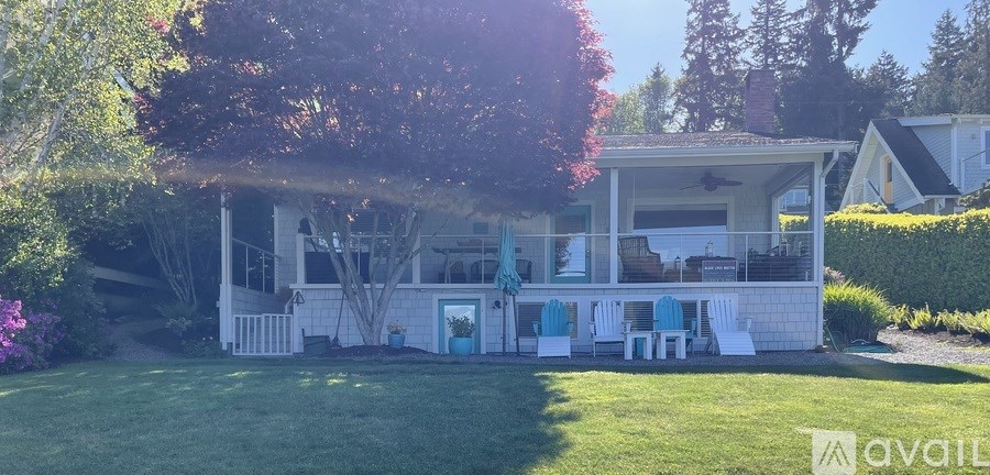 A house with a white porch and blue door is surrounded by greenery.