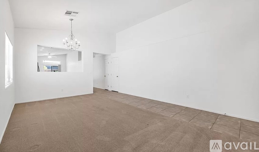 A large empty room with a carpeted floor and a chandelier hanging from the ceiling.