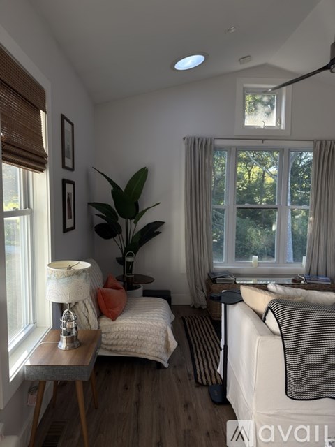 A well-lit bedroom with a bed, a table with a lamp, and a window with curtains.