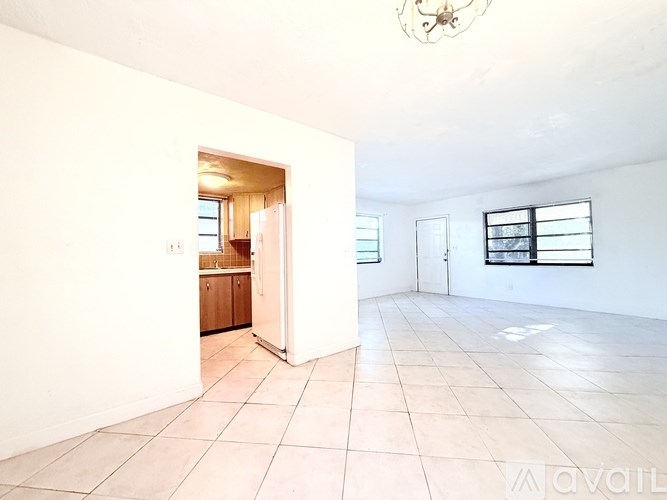 A room with a white wall and a doorway leading to a kitchen.