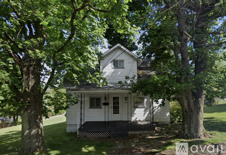 A white house with a porch is surrounded by trees.