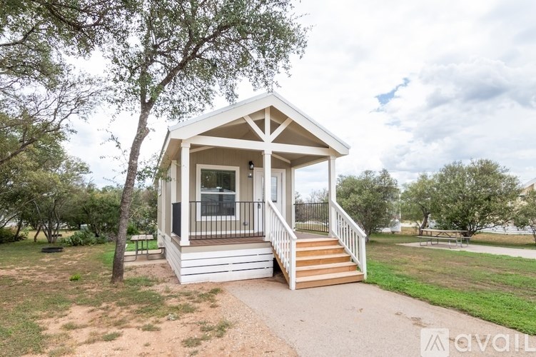 A small white house with a porch and a tree in front.