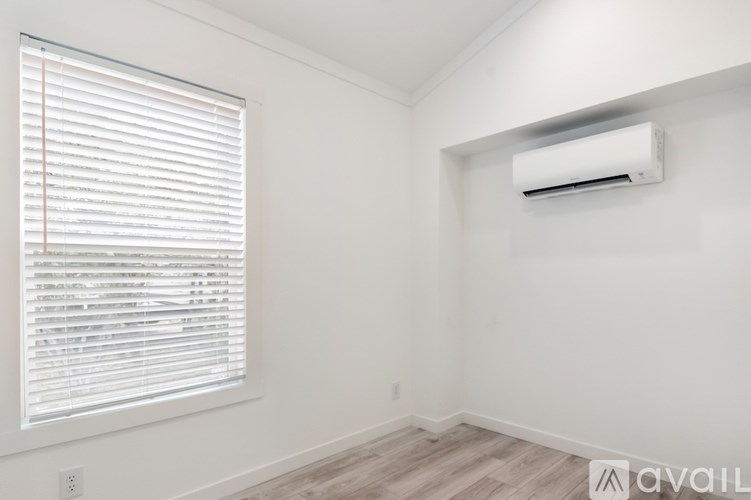 A room with a window covered by white blinds and a wall-mounted air conditioner unit.