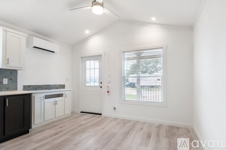 A well-lit, empty room with a kitchen area to the left and a door to the right.