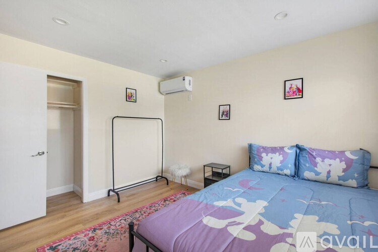 A bedroom with a bed, a rug, a small table, and a hanging clothes rack.