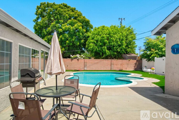 A patio with a table, chairs, and an umbrella overlooking a pool.