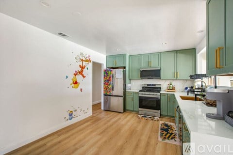 A kitchen with green cabinets and a white wall with drawings on it.