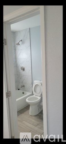 A white toilet is in a bathroom with a white tub and a white shower curtain.