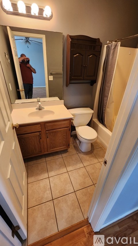 A man is taking a picture of a bathroom with a sink, toilet, and shower.