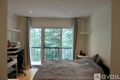 A bedroom with a large bed and a balcony with a view of trees.