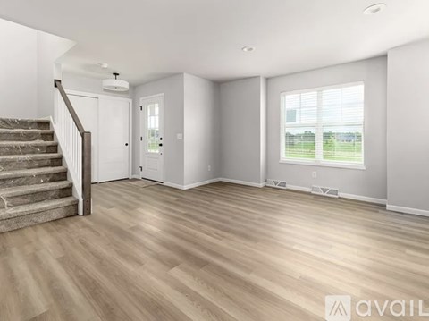 A spacious room with wooden flooring and a staircase leading to the upper level.