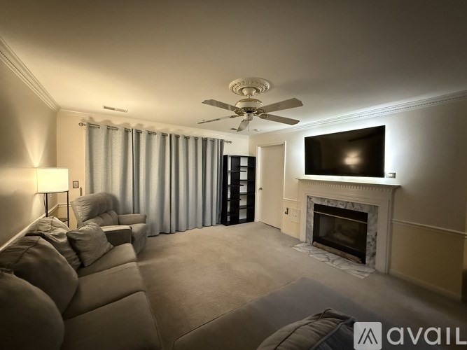 A living room with a grey couch, a fireplace, a television, and a ceiling fan.