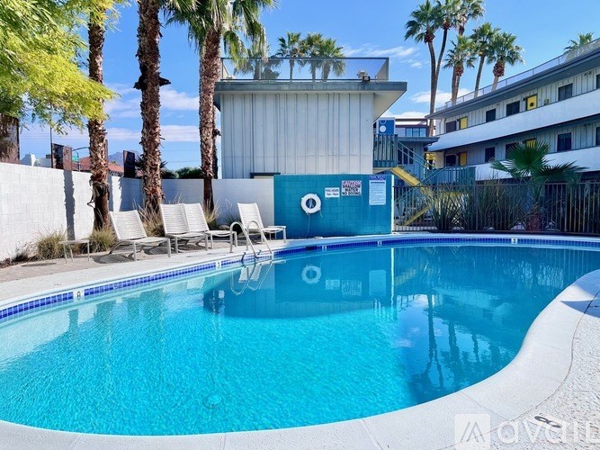 A pool surrounded by palm trees and a white building.