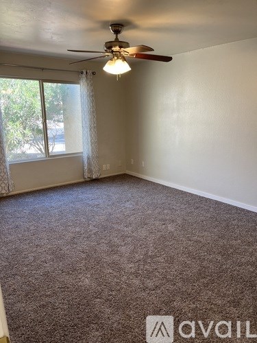 A room with a carpeted floor, a ceiling fan, and a window with curtains.