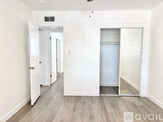 A white hallway with wood flooring and a door on the left.