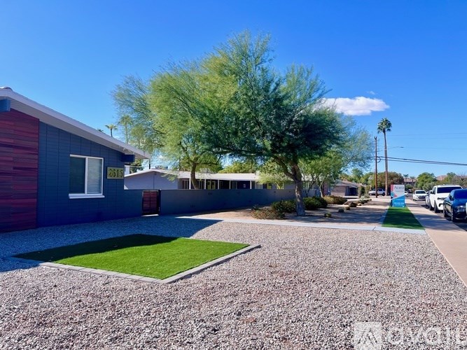 A blue house with a gravel driveway and a green tree in front.