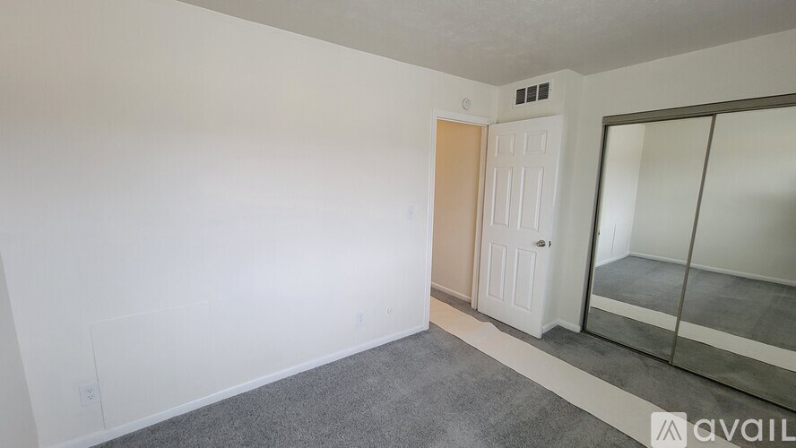 A room with a carpeted floor, a white door, and a mirrored wall.
