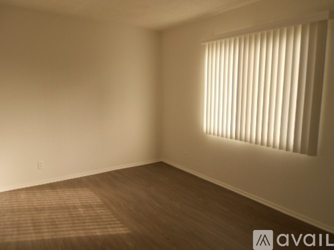 A room with a window covered by white blinds and wooden flooring.