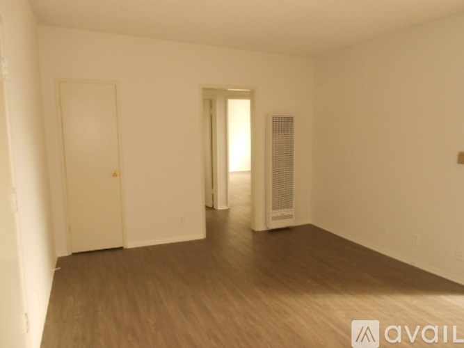 A room with wooden floors and white walls, with a door on the left and a window on the right.
