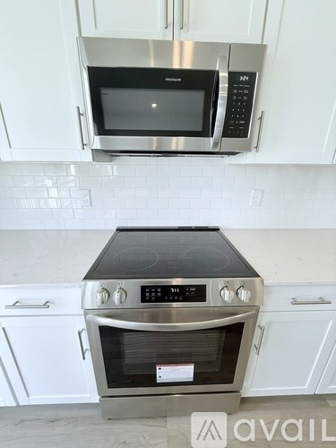 A stainless steel oven with a black glass door is in a kitchen with white cabinets.
