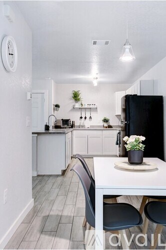 A kitchen with a black refrigerator, white cabinets, and a white table with a plant on it.
