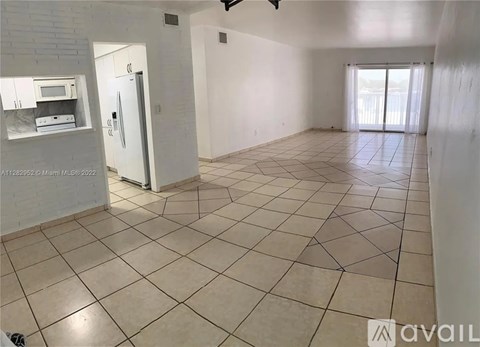 A spacious room with tiled flooring and a sliding glass door leading to a balcony.