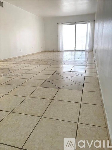 A spacious room with tiled flooring and a sliding glass door.