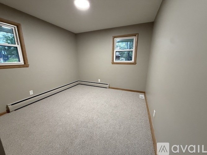 A room with a carpeted floor, two windows, and a picture frame on the wall.