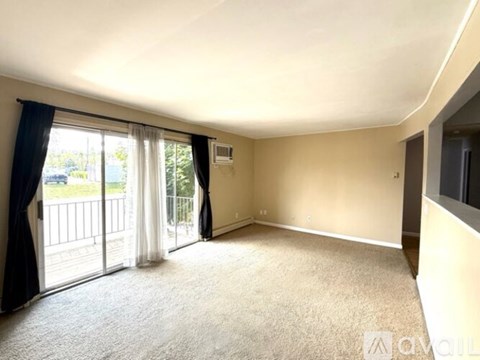 A spacious room with a carpeted floor and sliding glass doors leading to a balcony.
