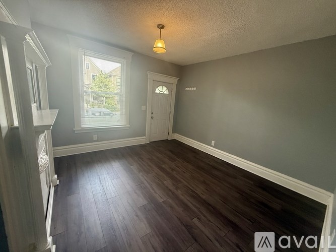 A room with wooden flooring and a window showing a view of a house.