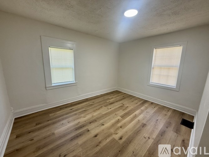 A room with wooden flooring and two windows.
