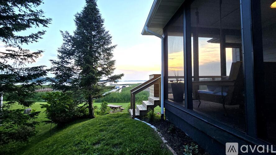 A house with a balcony overlooks a green lawn and trees.