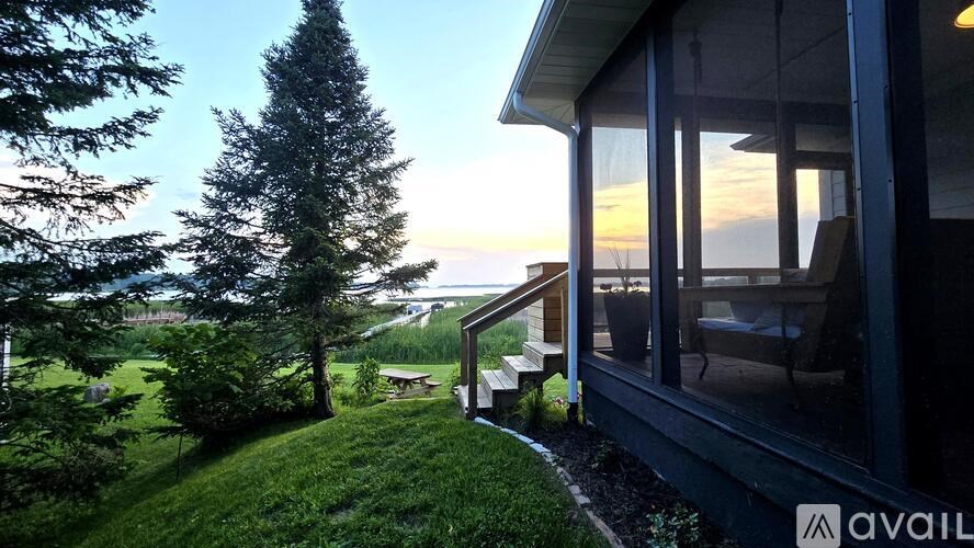 A house with a balcony overlooks a green lawn and trees.