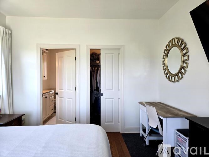 A bedroom with a bed, desk, and mirror.