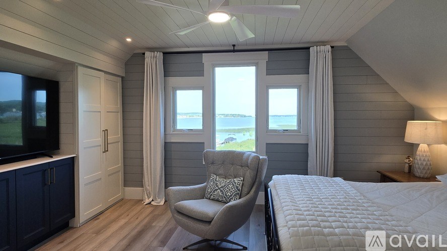 A bedroom with a bed, chair, and a window overlooking the water.