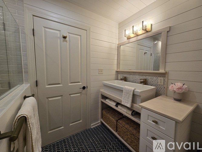 A bathroom with a white door, sink, and mirror.
