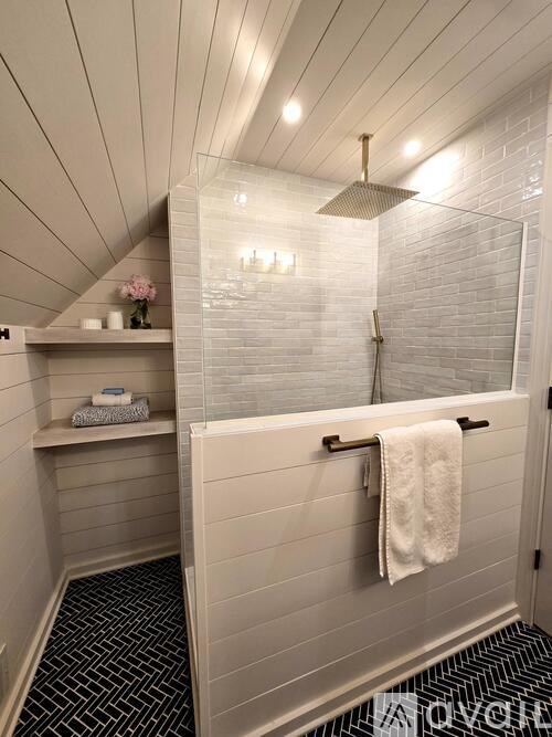 A bathroom with a white tiled shower and a black and white floor.