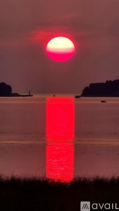 The sun is setting over a body of water, casting a red glow on the horizon.