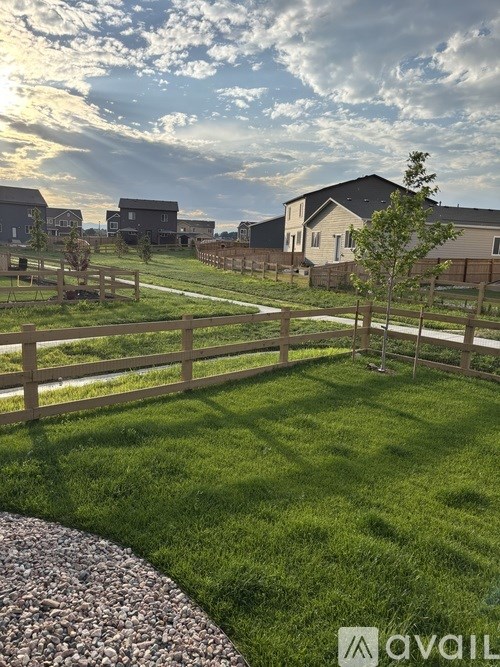 A grassy area with a fence and a tree in the foreground with houses in the background.