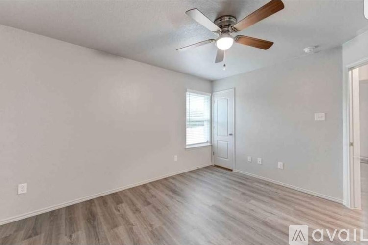 A room with a ceiling fan and light fixture, wooden flooring, and two doors.
