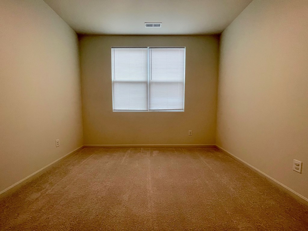 A room with a carpeted floor and a window with blinds.