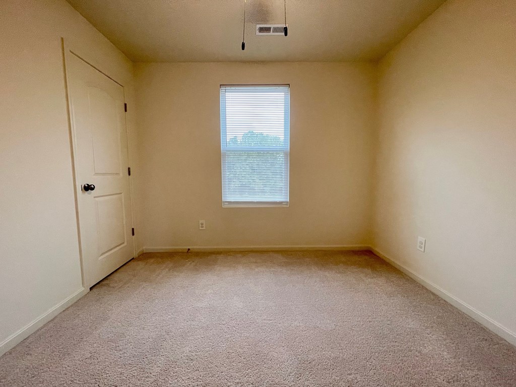 A room with a carpeted floor, a window, and a door.