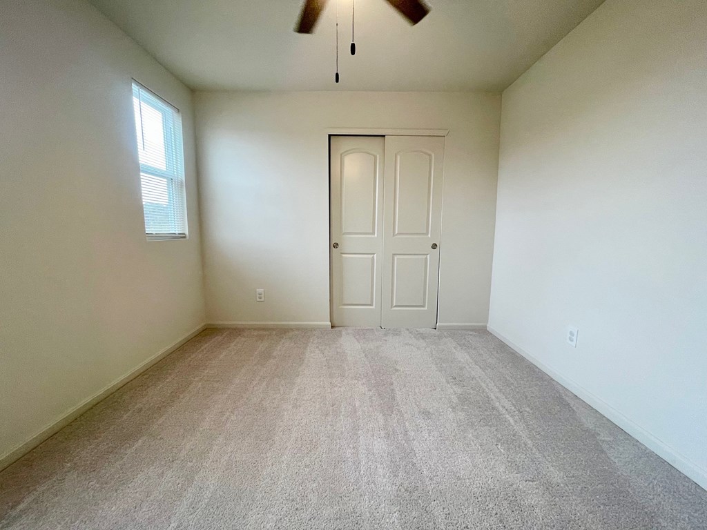 A room with a carpeted floor, a ceiling fan, and a door.