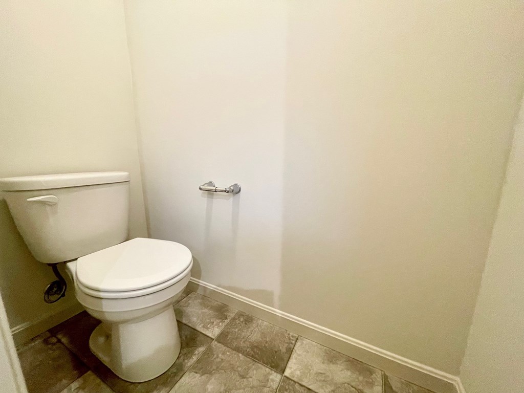 A white toilet sits next to a white wall in a bathroom.