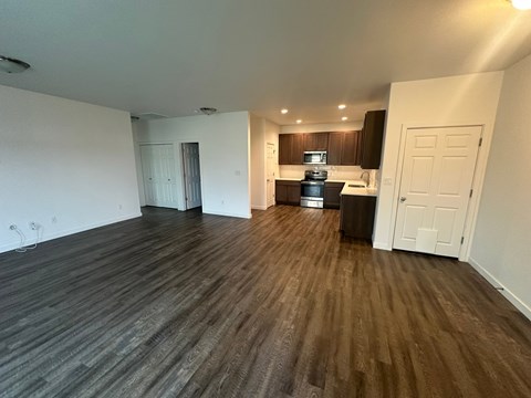 A room with wooden flooring and a kitchen area in the background.